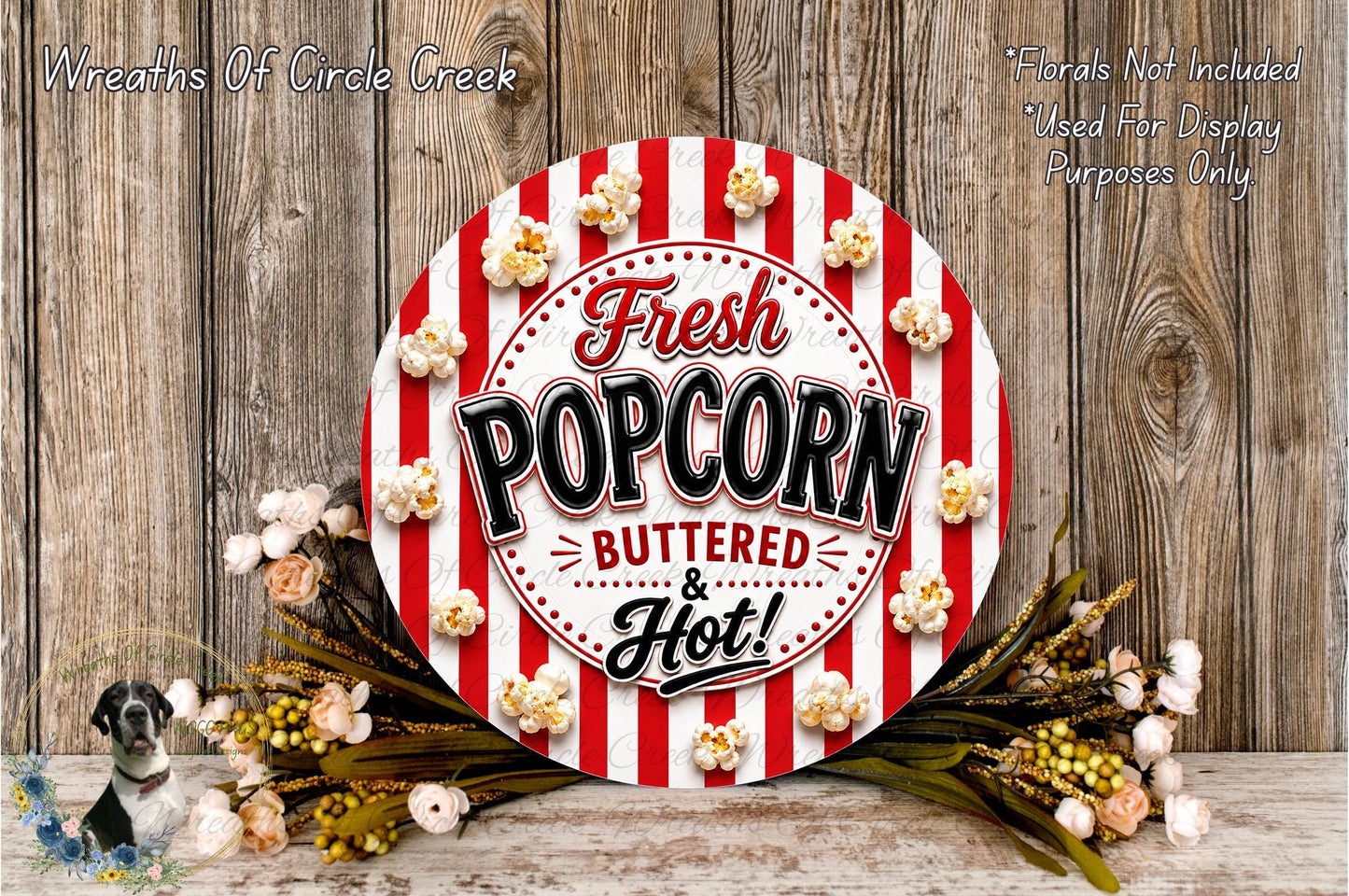 a circular sign with the text "Fresh Popcorn Buttered & Hot!" surrounded by popcorn and flowers, placed on a wooden surface.