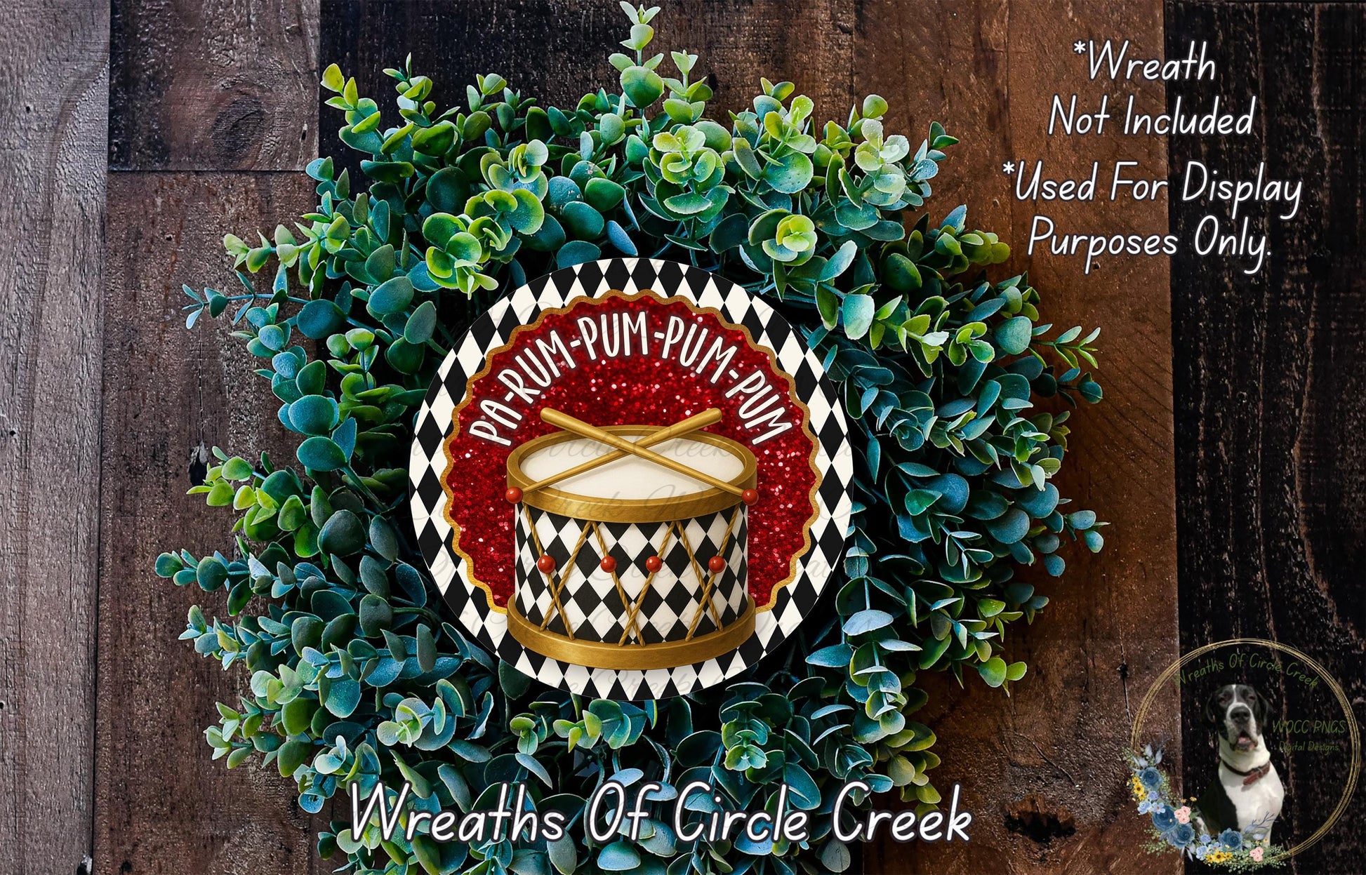 A wreath made of green and red foliage, with a red and gold drum design in the center. The wreath is displayed on a wooden surface, and there is a text overlay that reads "Wreath Not Included * Used For Display Purposes Only" and "Wreaths Of Circle Creek".