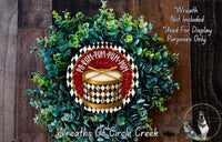 A wreath made of green and red foliage, with a red and gold drum design in the center. The wreath is displayed on a wooden surface, and there is a text overlay that reads "Wreath Not Included * Used For Display Purposes Only" and "Wreaths Of Circle Creek".