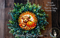 A wreath made of green leaves and a carved pumpkin, featuring a cartoon cow and a carved jack-o-lantern.