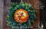 A wreath made of green leaves and a carved pumpkin, featuring a cartoon cow and a carved jack-o-lantern.