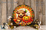 A decorative wreath featuring a large pumpkin and a cow, surrounded by autumn foliage and candy corn, placed on a wooden surface.