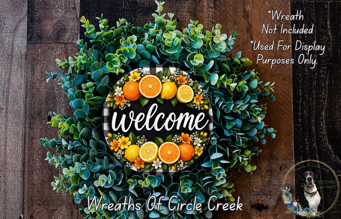 a wreath made of various greenery, including eucalyptus and other plants, with a sign that says "Welcome" in the center. The wreath is displayed on a wooden surface, and there is a small dog in the bottom right corner.