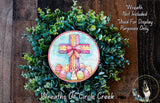 a wreath with a cross and Easter eggs, surrounded by greenery. The wreath is displayed on a wooden surface, and there is a small dog in the bottom right corner of the image.