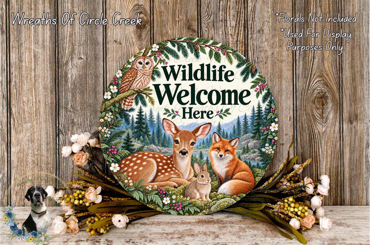 A round sign with a forest scene featuring deer, fox, and rabbit, surrounded by flowers and greenery. The sign reads "Wildlife Welcome Here".
