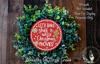 A wreath made of green leaves and a red circular sign with the text &quot;Let&#39;s Bake Stuff & Watch Christmas Movies&quot; is displayed on a wooden background.