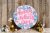 A round floral wreath with the text "Happy Mother's Day" written on it, surrounded by various flowers and greenery.