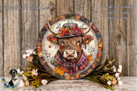 A decorative plate featuring a cow wearing a plaid scarf and a hat with flowers, surrounded by autumn foliage and flowers on a wooden surface.