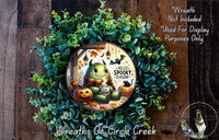 A wreath made of green leaves and a carved pumpkin, featuring a cartoon monster with a friendly expression and the text "Hello Spooky Season!"