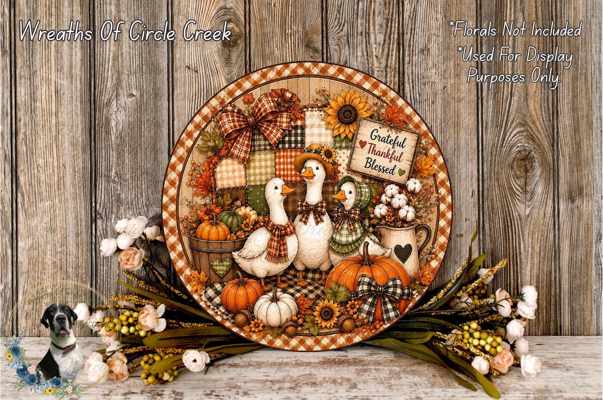 A decorative wreath featuring a group of white geese, pumpkins, and other fall-themed elements, surrounded by flowers and placed on a wooden surface.