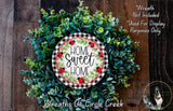 a wreath made of various green plants and flowers, with a decorative sign that reads "Home Sweet Home" in the center.