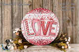 a decorative sign with the word "LOVE" written on it, surrounded by a wreath of flowers and a wooden background.