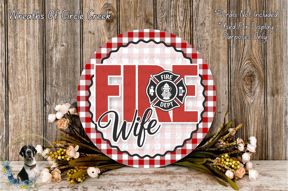 a round sign with the text "FIRE WIFE" in a red and white checkered pattern, surrounded by a floral arrangement and a wooden background.