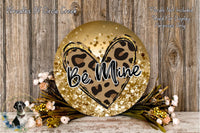 a decorative sign with a leopard print heart and the word "Be Mine" written on it, surrounded by a floral arrangement and placed on a wooden surface.