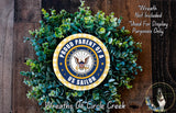 A wreath made of green leaves and a circular emblem with the text "Proud Parent of a US Sailor" and the United States Navy seal emblem, placed on a wooden surface.