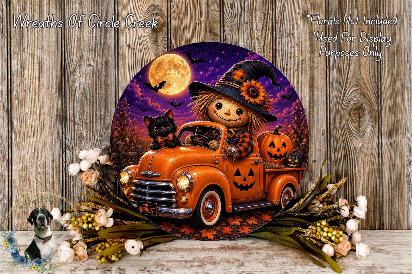 A Halloween-themed wreath featuring a scarecrow in a witch's hat driving an orange truck, with jack-o-lanterns and flowers on the side.