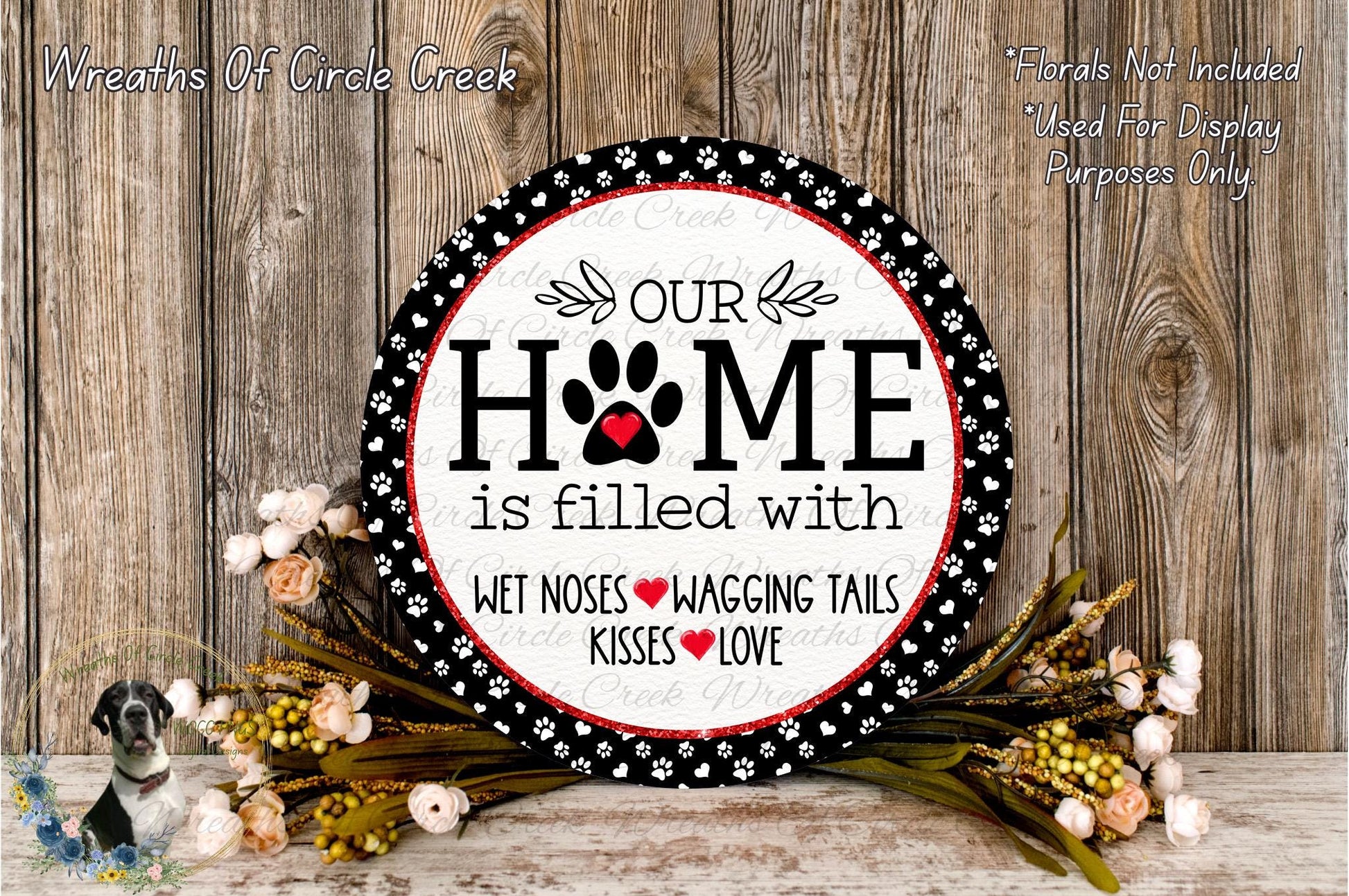 A decorative sign with the text "Our Home is filled with WET Noses WAGGING Tails KISSES LOVE" surrounded by a floral arrangement on a wooden surface.
