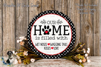 A decorative sign with the text "Our Home is filled with WET Noses WAGGING Tails KISSES LOVE" surrounded by a floral arrangement on a wooden surface.