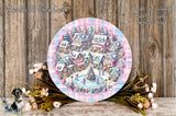 A decorative plate featuring a winter village scene with colorful houses, trees, and a Christmas tree, surrounded by flowers and placed on a wooden surface.