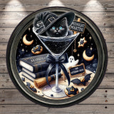 A black cat wearing a witch's hat is sitting in a martini glass, surrounded by Halloween-themed objects such as a book, broom, ghost, and bats.