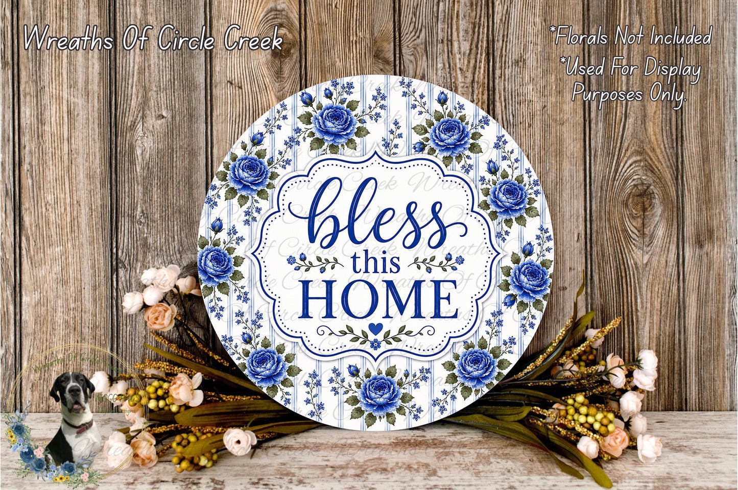 a decorative sign with the text "Bless this home" surrounded by blue flowers and greenery. The sign is placed on a wooden surface, and there are additional floral arrangements in the background.