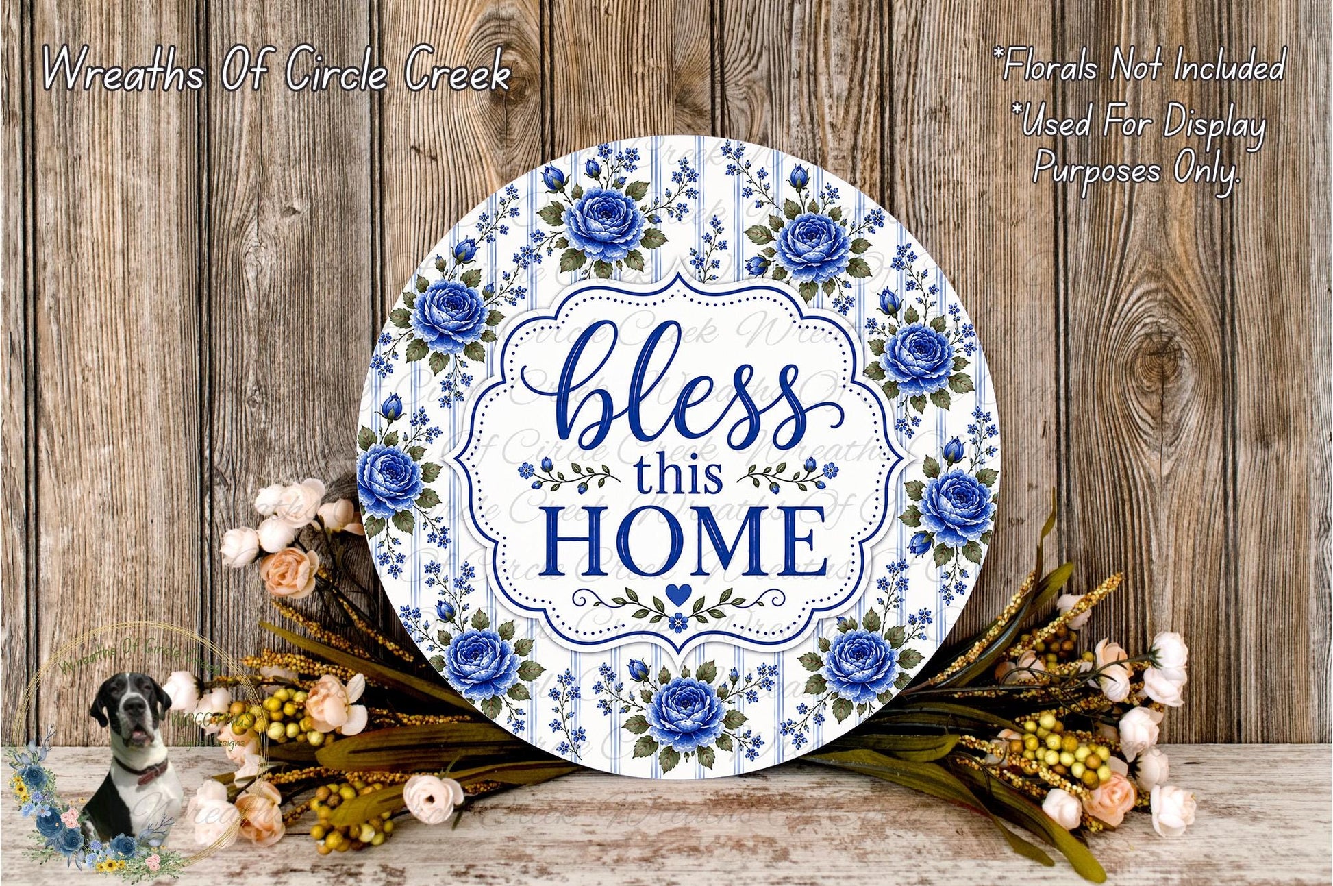a decorative sign with the text "Bless this home" surrounded by blue flowers and greenery. The sign is placed on a wooden surface, and there are additional floral arrangements in the background.