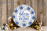 a decorative sign with the text "Bless this home" surrounded by blue flowers and greenery. The sign is placed on a wooden surface, and there are additional floral arrangements in the background.