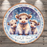 A circular wooden plaque with a snowy winter scene featuring three white cows with horns, wearing festive accessories and the text "Let it Snow" at the bottom.