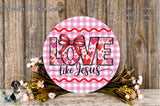 a round sign with the text "LOVE like Jesus" written on it, surrounded by a floral arrangement and a wooden background.