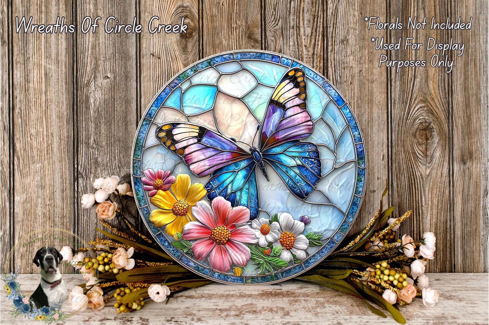 A stained glass-style wreath with a butterfly design, surrounded by colorful flowers and placed on a wooden surface.