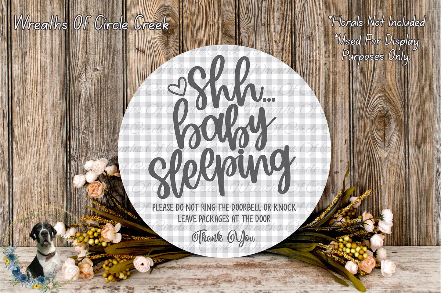 a round sign with a floral design and text, placed on a wooden surface. The sign reads "Shh... baby sleeping" and includes a warning not to ring the doorbell or knock on the door, and to leave packages at the door.