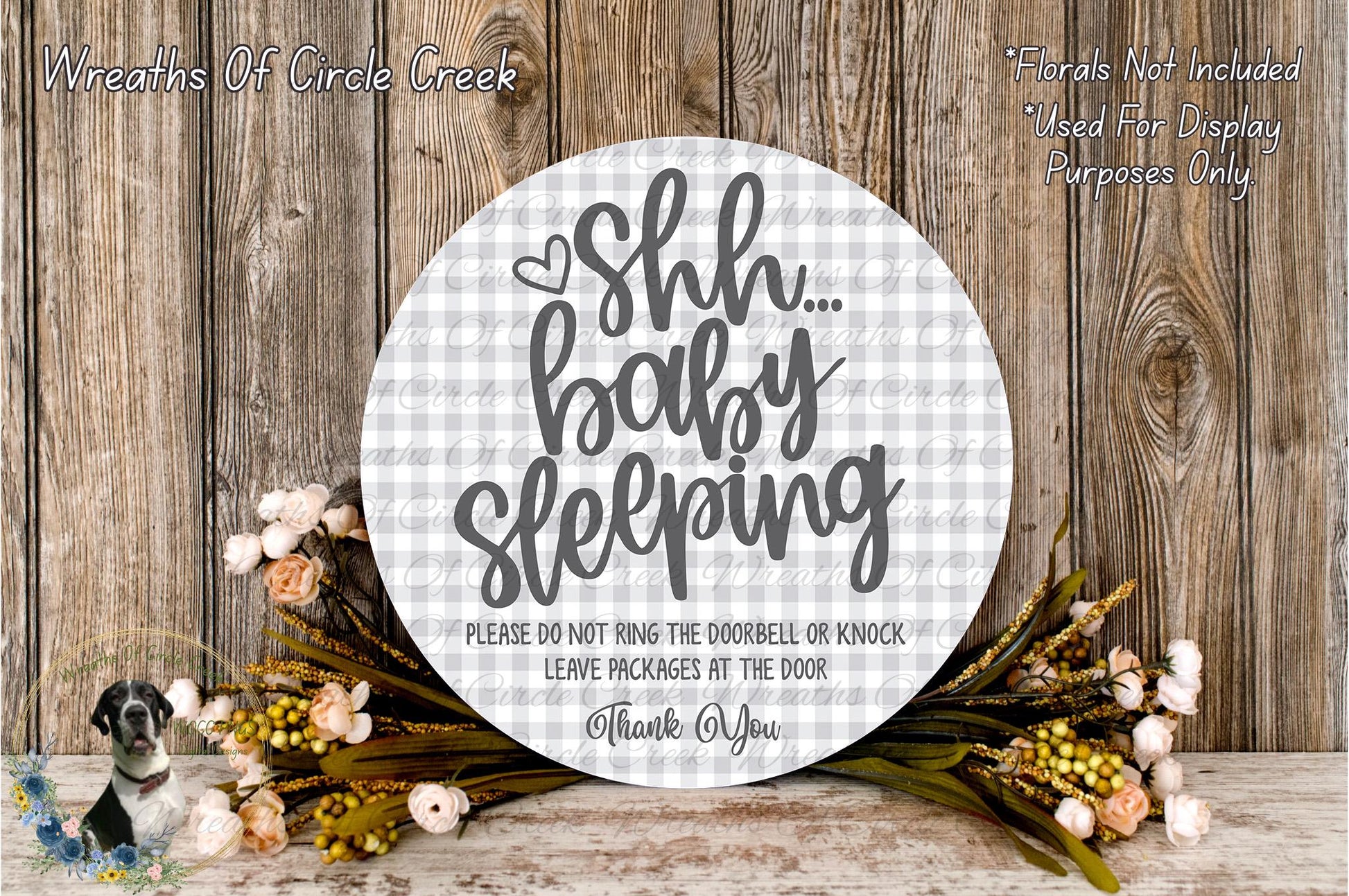 a round sign with a floral design and text, placed on a wooden surface. The sign reads "Shh... baby sleeping" and includes a warning not to ring the doorbell or knock on the door, and to leave packages at the door.