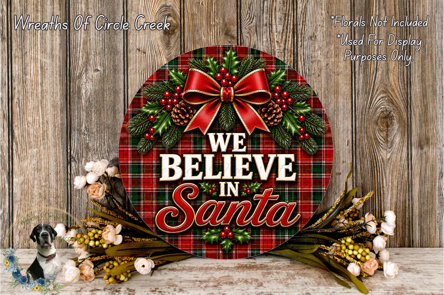A festive wreath with a red ribbon and a plaid pattern, surrounded by flowers and greenery, with the text "We Believe in Santa" displayed on it.
