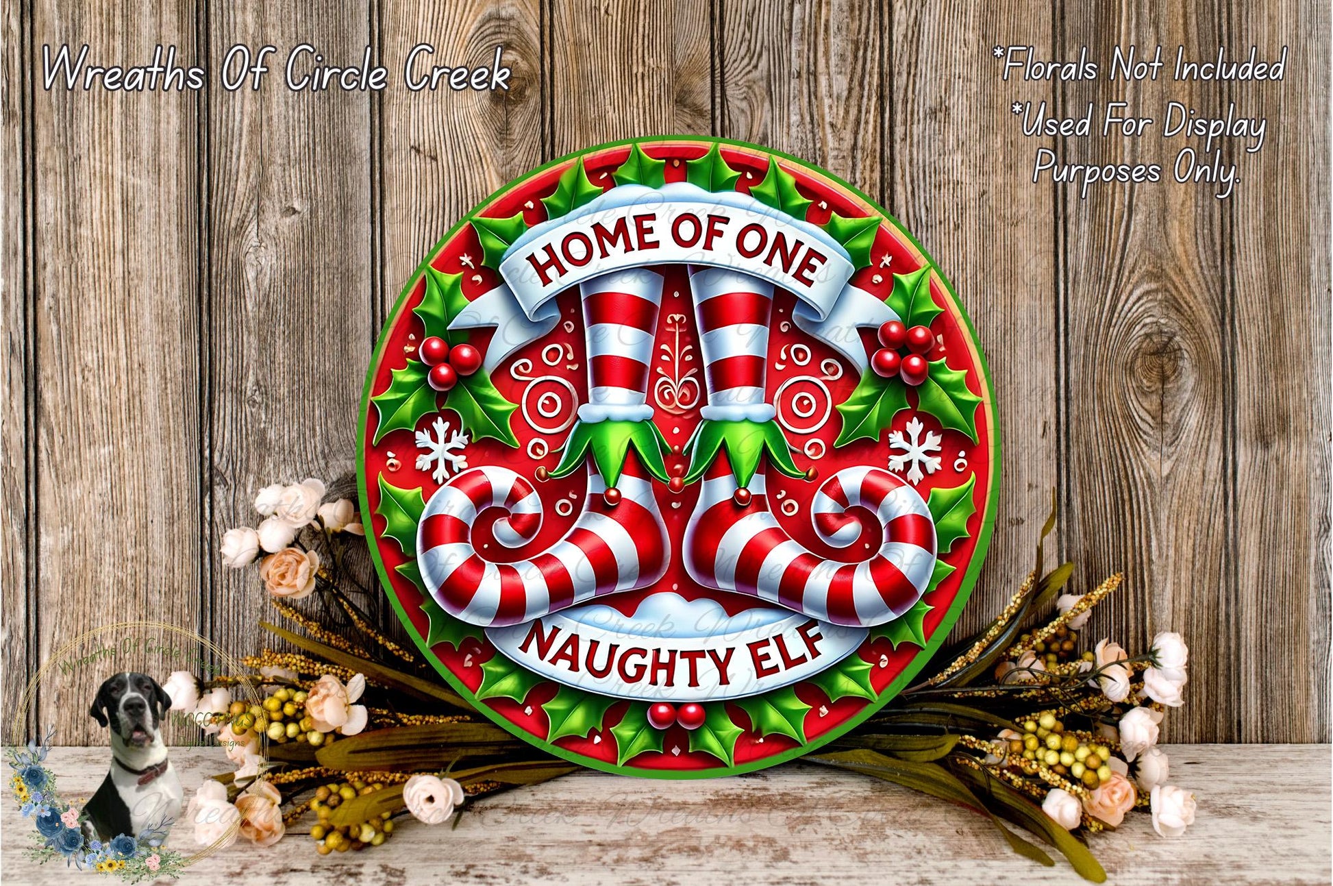 a festive wreath with the text "HOME OF ONE Naughty Elf" and a Santa Claus figurine. The wreath is displayed on a wooden surface, surrounded by flowers and greenery.