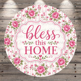 A round sign with a floral border and the text "bless this home" in pink and white.