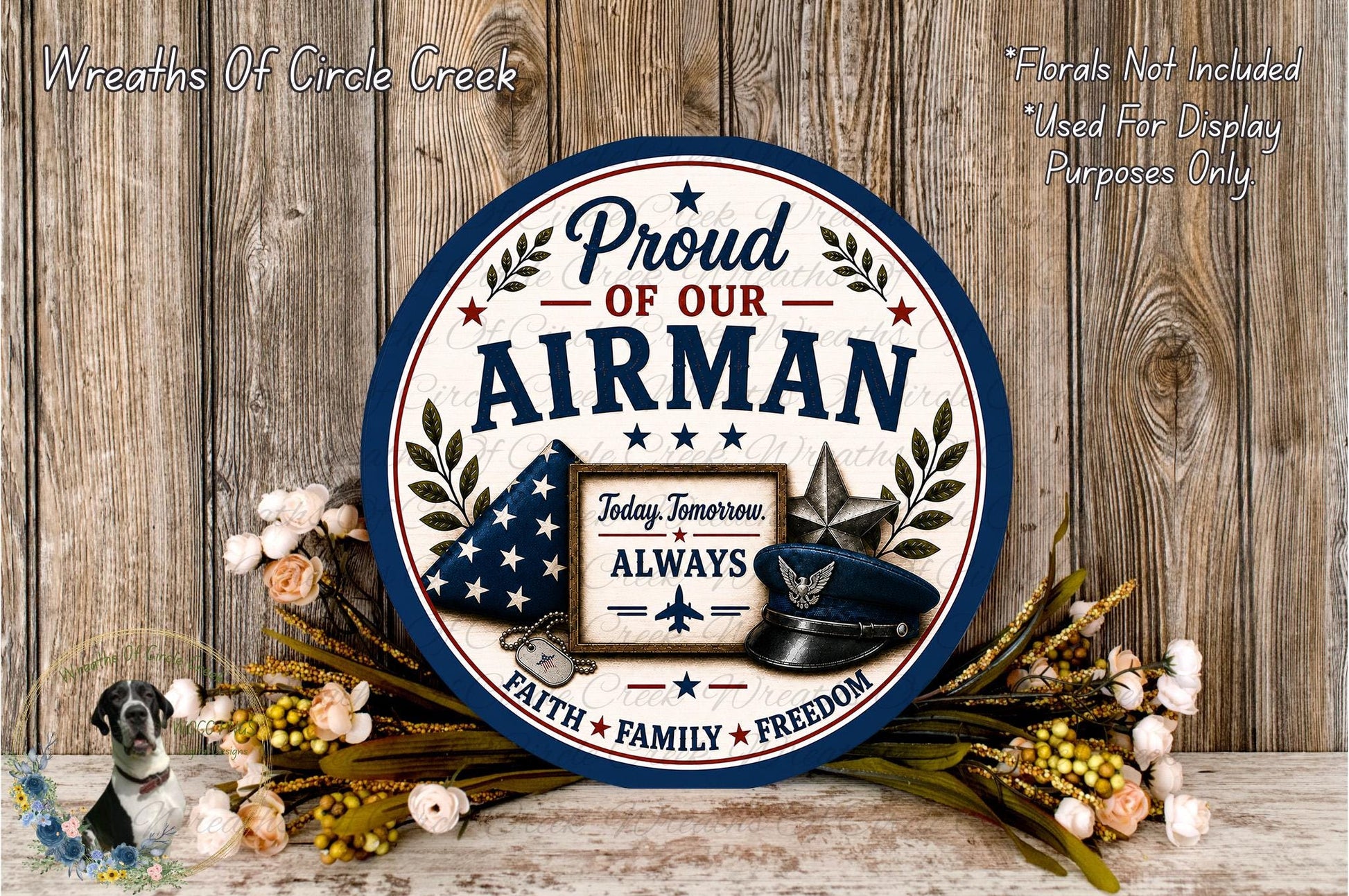 a patriotic sign with the text "Proud of our Airman" and a military-themed design, surrounded by flowers and a wooden background.