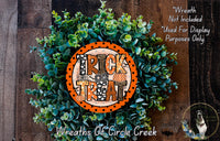 a wreath made of green foliage and an orange circular sign with the text "TRICK TREAT" on it, placed on a wooden surface.