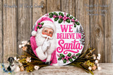 A round sign featuring a Santa Claus figure with the text "WE BELIEVE IN Santa" and surrounded by flowers and greenery.