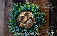 a wreath with a central image of a woman and a child, surrounded by a lush green plant. The wreath is displayed on a wooden surface, and there is a text overlay that reads "Wreath Not Included * Used For Display Purposes Only".