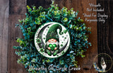 A wreath featuring a gnome wearing a green hat and holding a four-leaf clover, surrounded by a lush green plant.
