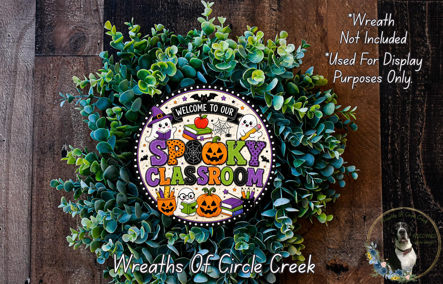 a wreath with a Halloween-themed design, including a sign that says "Welcome to our Spooky Classroom". The wreath is surrounded by green foliage, and there is a small dog in the bottom right corner of the image.
