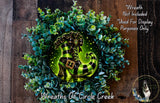 A wreath made of green and white eucalyptus leaves, with a glowing green shoe-shaped ornament in the center.