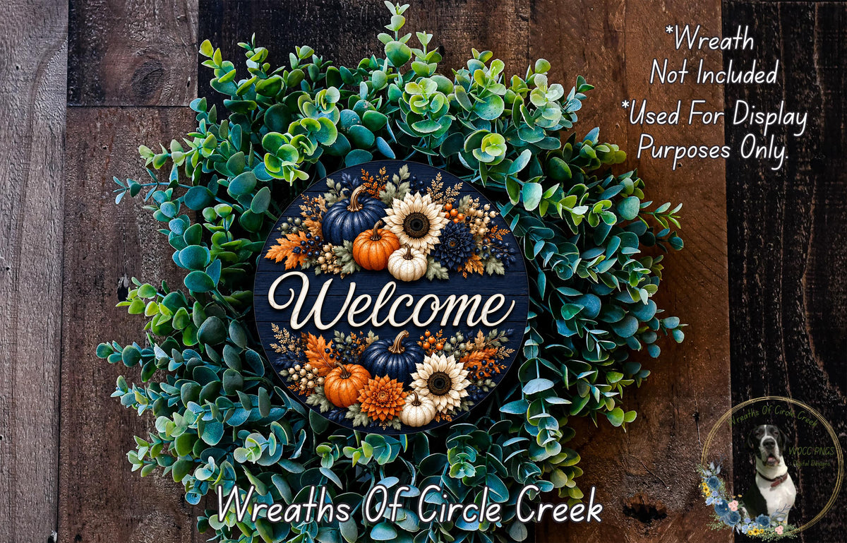 a wreath with a welcome sign in the center, surrounded by various fall-themed elements such as pumpkins, sunflowers, and greenery. The wreath is displayed on a wooden surface, and there is a small dog in the bottom right corner of the image.