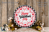 a round, decorative plate with a floral design and the text "Happy Valentine's Day" on it, placed on a wooden surface. There are also some flowers and greenery surrounding the plate.