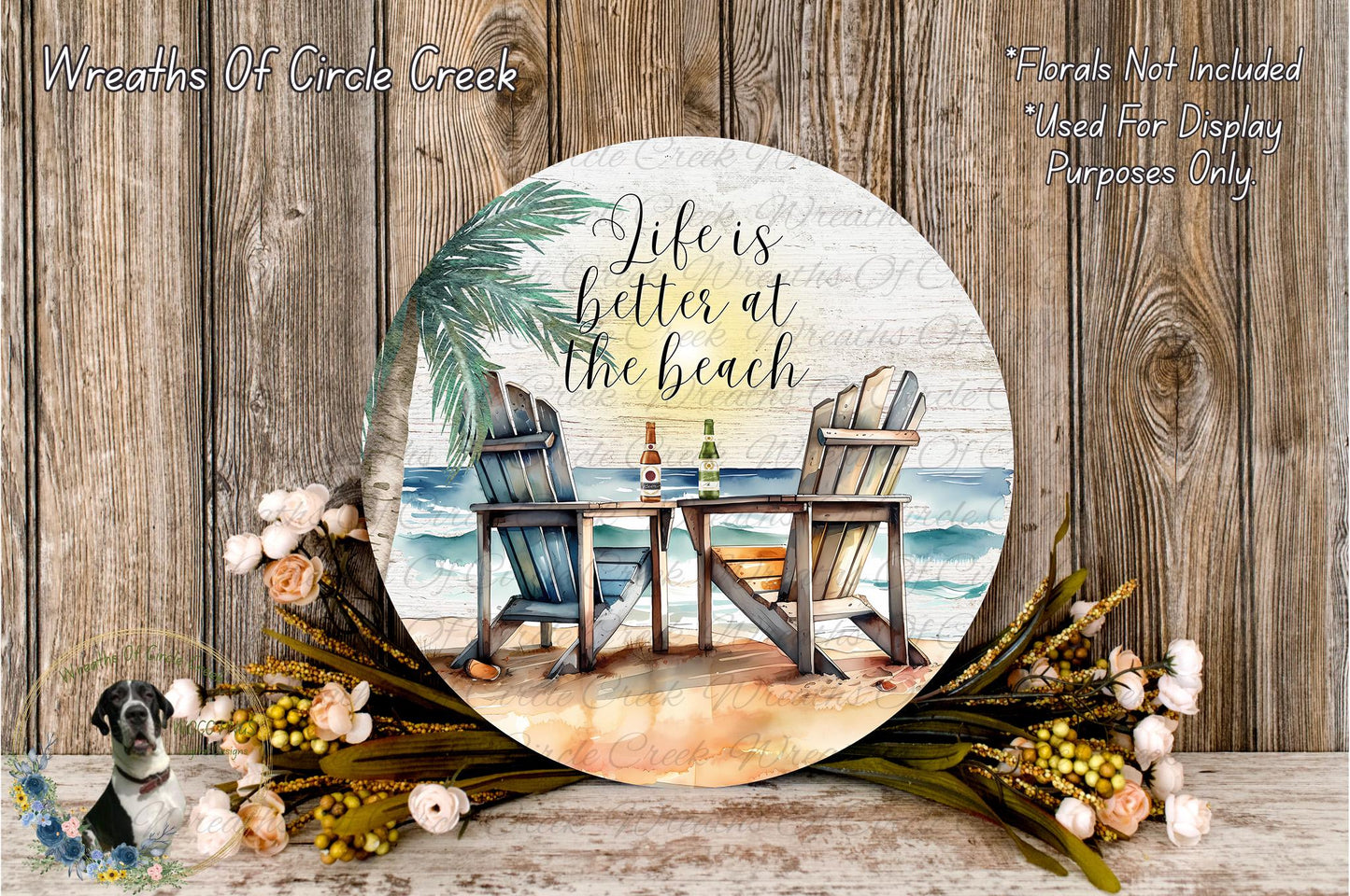 a round sign with a beach scene, including two beach chairs, a table, and a palm tree. The sign has a quote that says "Life is better at the beach" and is surrounded by flowers and greenery.