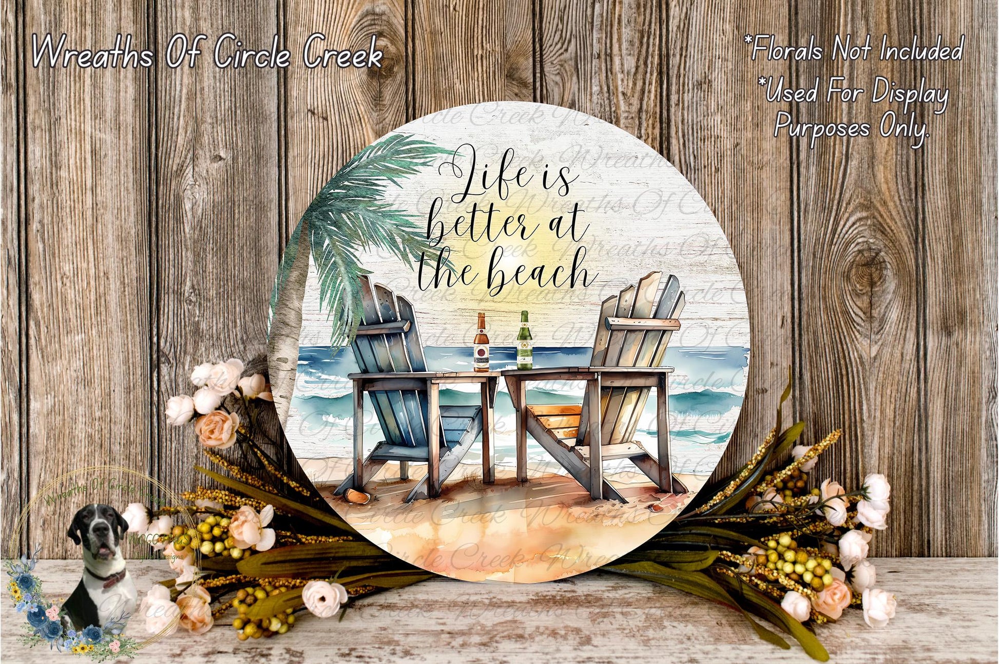 a round sign with a beach scene, including two beach chairs, a table, and a palm tree. The sign has a quote that says "Life is better at the beach" and is surrounded by flowers and greenery.