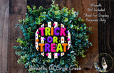 a wreath with the text "TRICK OR TREAT" in a colorful, decorative font. The wreath is made of green leaves and has a wooden background.