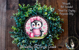 A wreath featuring a cute penguin wearing a pink and white checkered dress, surrounded by green foliage.
