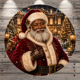 A smiling, bearded man dressed as Santa Claus, wearing a red velvet suit and carrying a sack of presents, stands in front of a beautifully decorated Christmas tree and building.