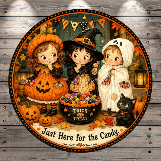 A Halloween-themed illustration featuring three young girls dressed in costumes, surrounded by pumpkins, candy, and a black cat, with the text "Just Here for the Candy" at the bottom.